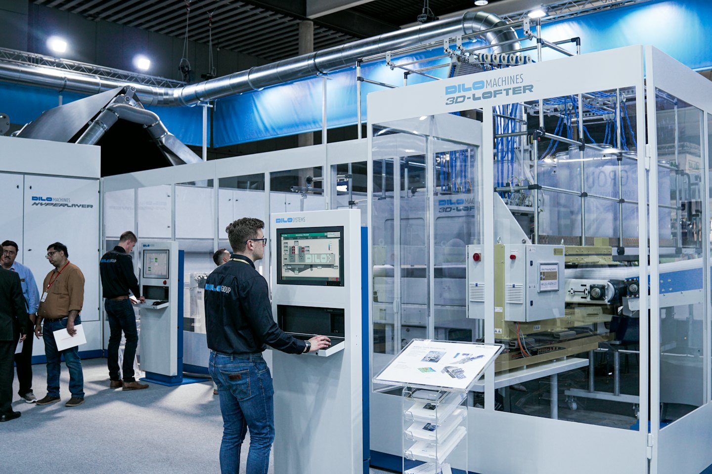 Professionals interact with textile machinery at an indoor trade show.
